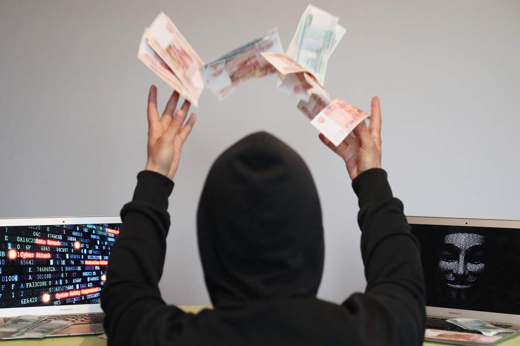 мошенник рдуется ворованным деньгам подкидывая их вверх над столом с ноутбуками