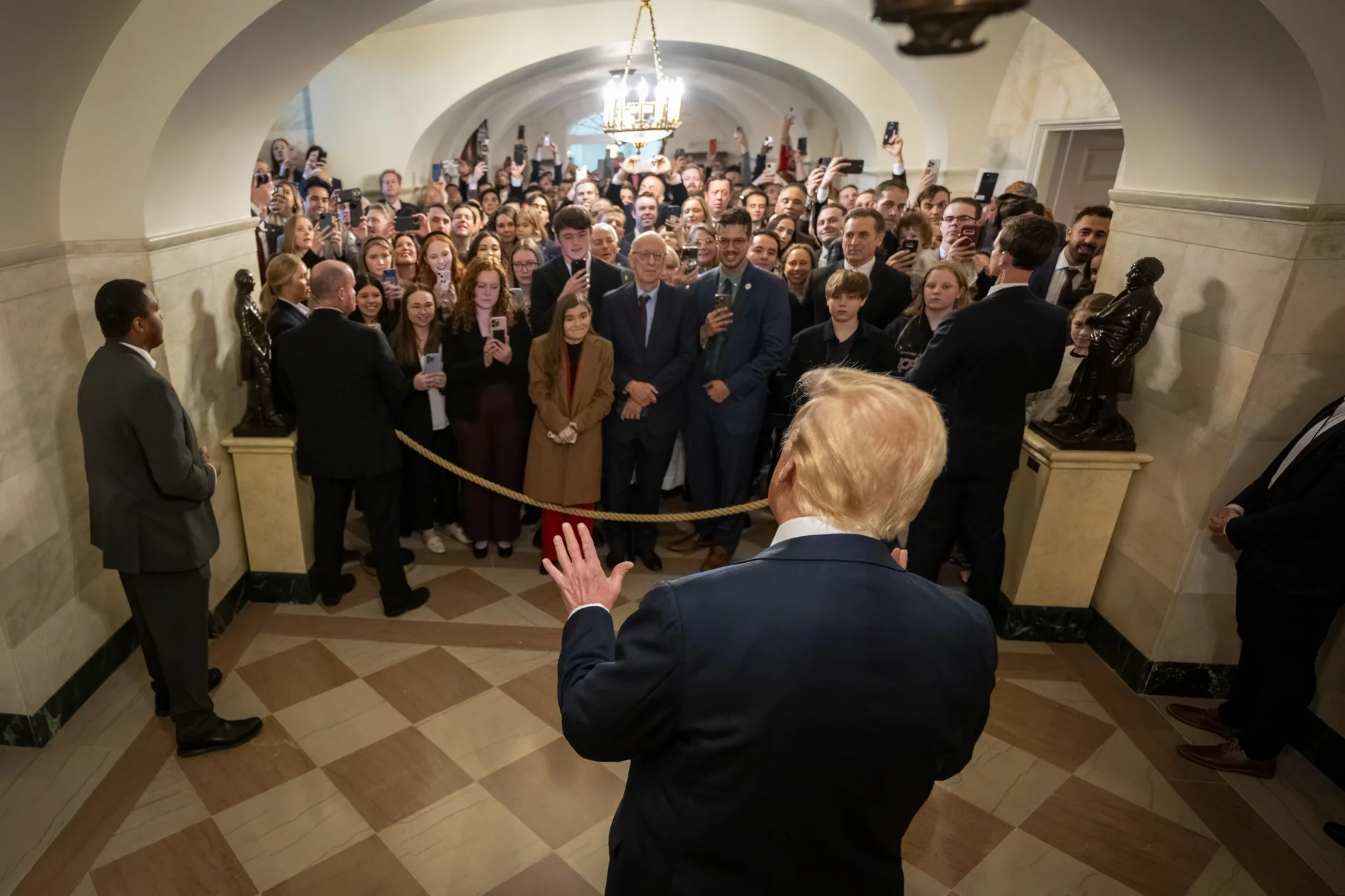 U.S. President Donald Trump stands in front of a crowd in a hall in the White House