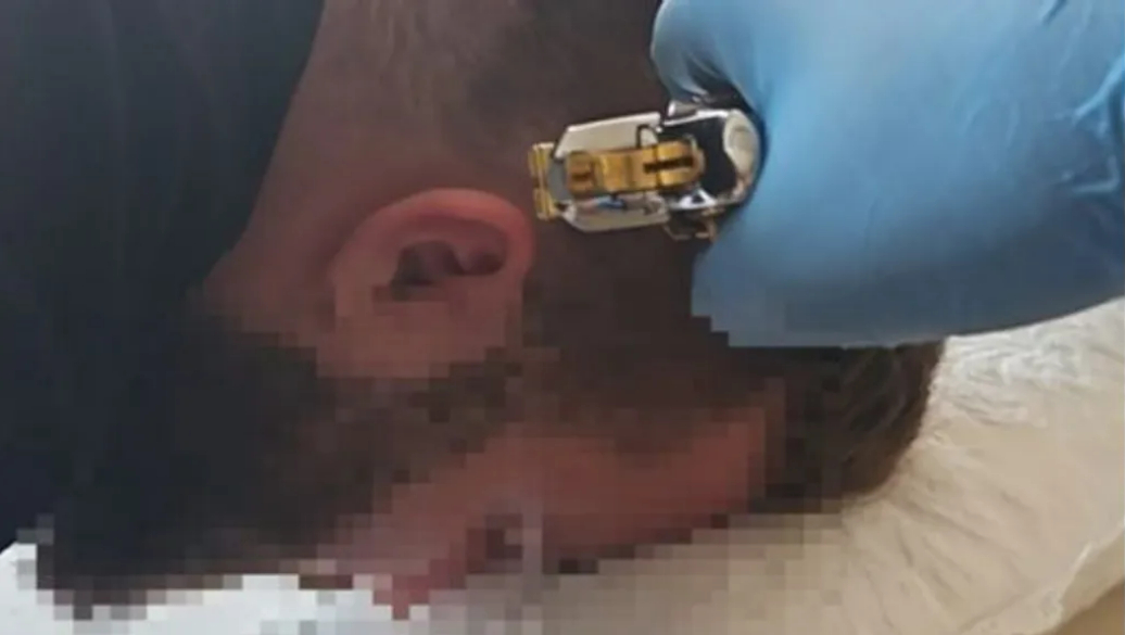 A man, whose face has been blurred, is held with a gun held to his head.