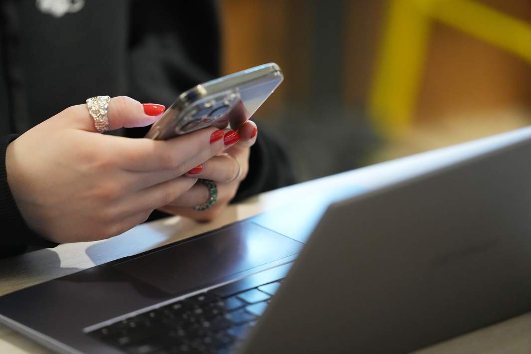 девушка сидит в телефоне на столе ноутбук